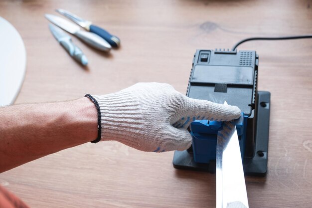 Thuis een mes slijpen op een elektrische slijper De hand van de man drijft het mes tussen de blauwe slijpers stofvliegen op de machine