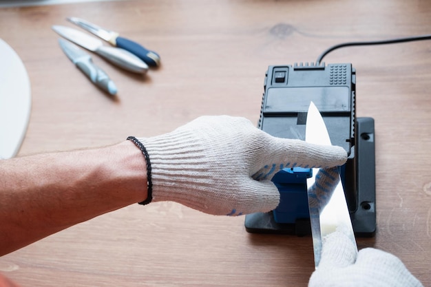 Thuis een mes slijpen op een elektrische slijper De hand van de man drijft het mes tussen de blauwe slijpers stofvliegen op de machine