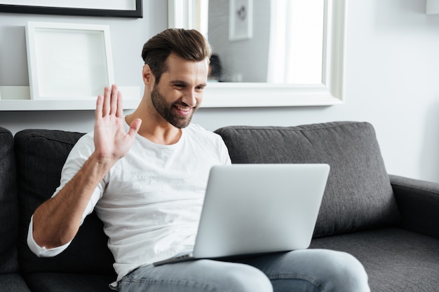 Thuis glimlachend jonge mensenzitting binnen terwijl het gebruiken van laptop