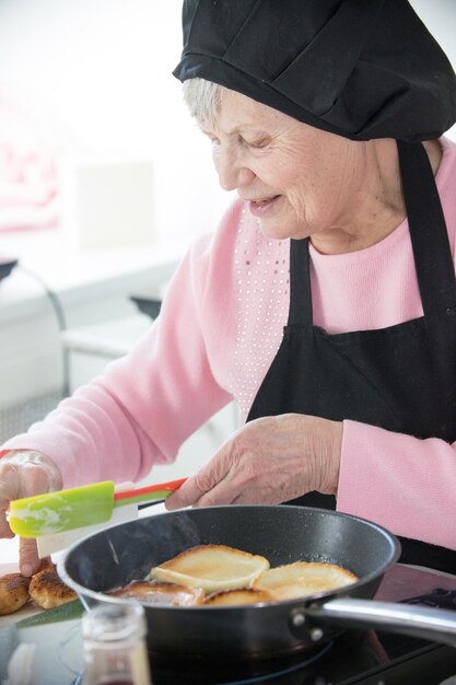 Thuis keuken een oude vrouw die pannenkoeken maakt