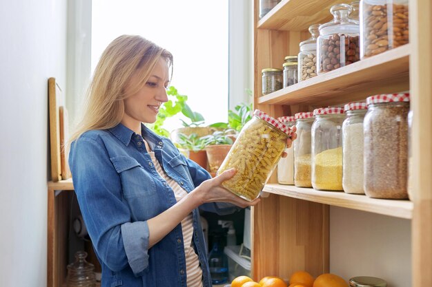 Thuis keuken pantry vrouw in de buurt van houten rek met voedsel in potten en containers