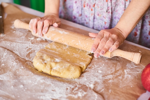 Thuis koken. Handen die met het receptbrood werken van de deegvoorbereiding. Vrouwelijke handen maken van deeg voor pizza. De handen van de vrouw rollen het deeg. Moeder rolt deeg op het bord van de keuken met een deegroller