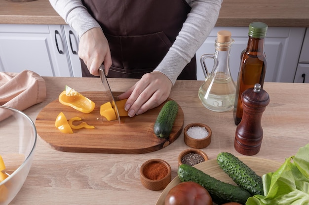 Thuis koken van heerlijk gezond vegetarisch eten in de keuken, de handen van het meisje snijden verse paprika's op een snijplank