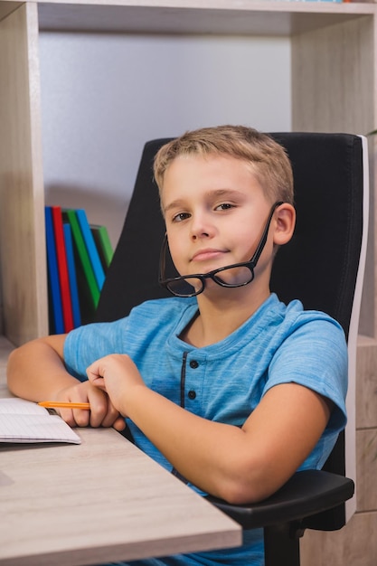 Thuis leren online onderwijs Schooljongen met bril studeert thuis Boy kijkt naar de camera