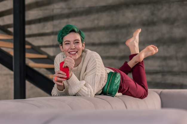 Thuis relaxen. Stralende vrouw met groene ogen die thuis op de bank aan het chillen is terwijl ze op haar vriendje wacht