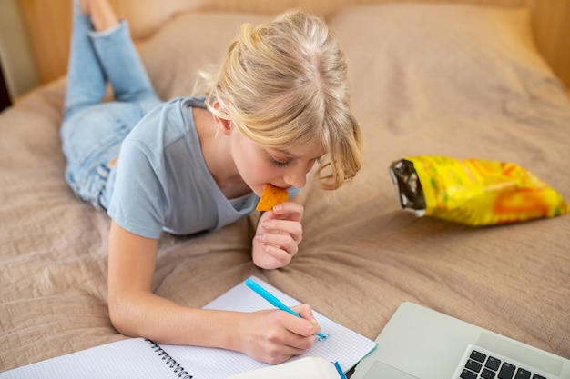 Thuis studeren. Een tienermeisje dat op het bed ligt en haar lessen doet