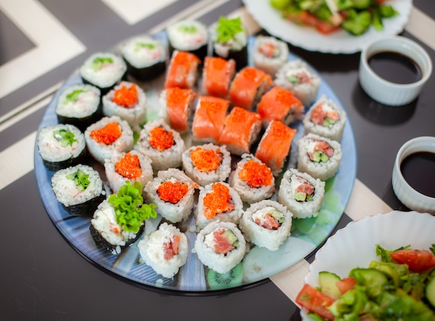 Thuis sushi en broodjes maken. Sushi met zeevruchten, salade en witte rijst. Eten voor familie en vrienden. Een set van verschillende broodjes en sushi op een dienblad.