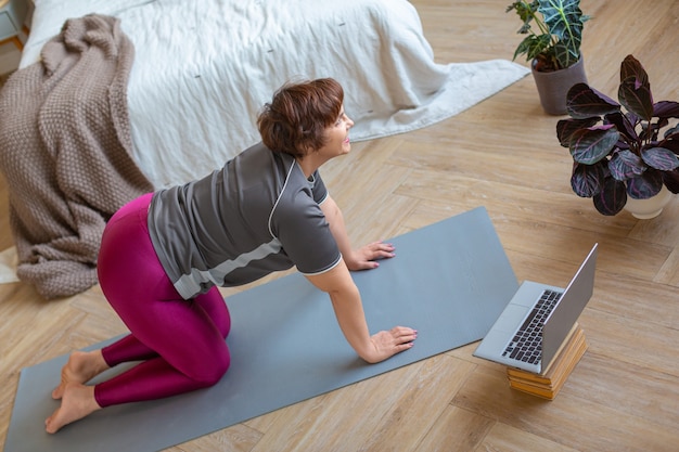 Thuis trainen senior vrouw die thuis traint voor een laptopmonitor die zich uitstrekt