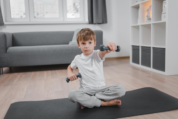 Thuis training. Portret van een jongen die traint met halters terwijl hij op de vloer van de woonkamer zit.