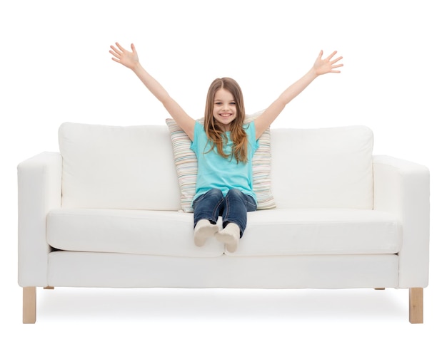 thuis, vrije tijd en geluk concept - glimlachend klein meisje zittend op de bank en zwaaiende handen