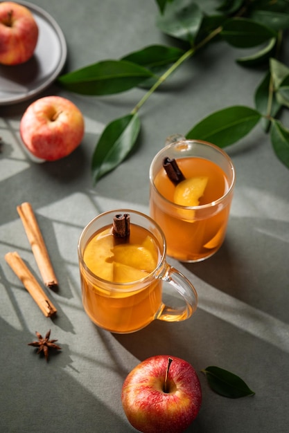 Thuisgemaakte appelpunch met verse appels kaneel en specerijen in bekers op een groene achtergrond met verse vruchten tak en ochtend schaduwen Een warme gezonde herfst drank