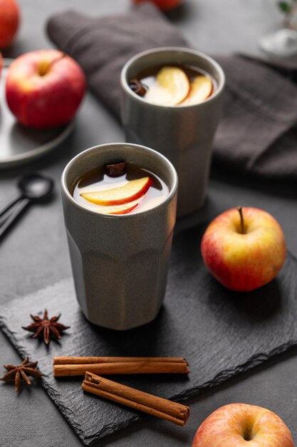 Foto thuisgemaakte appelpunch of cider met appels en kaneel in grijze bekers op een donkere achtergrond met vers fruit en specerijen dichtbij