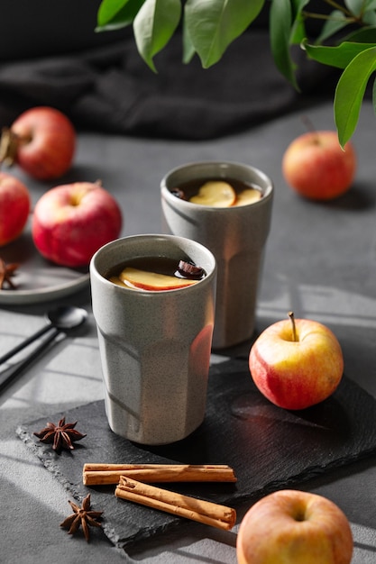 Foto thuisgemaakte appelpunch of cider met appels en kaneel in grijze bekers op een donkere achtergrond met verse vruchten, specerijen en schaduwen