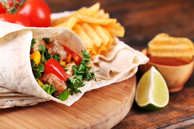 Thuisgemaakte smakelijke burrito met groenten en aardappelchips op snijplank op houten achtergrond