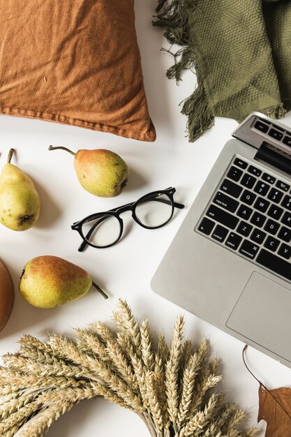 Thuiskantoor tafel bureau werkruimte met laptop, bril, krans van tarwestro, droge herfstbladeren, peren, deken, kussen. Plat leggen