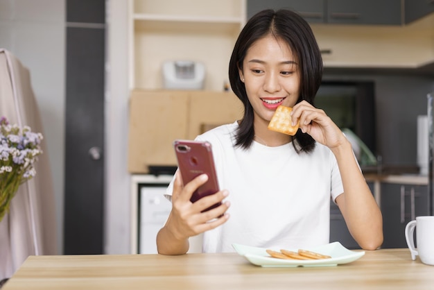Thuisontspanningsconcept Jonge vrouw die crackers eet en thuis op sociale media op smartphone surft