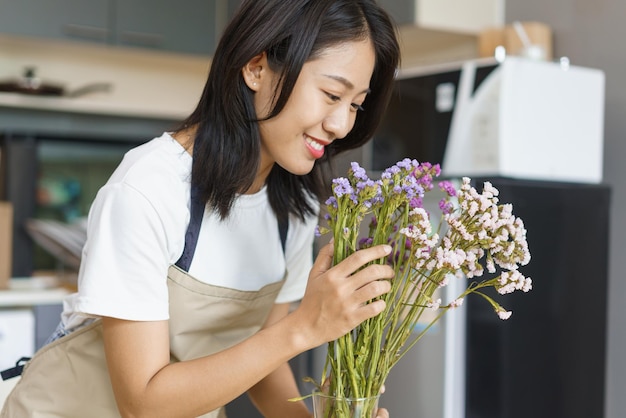Thuisontspanningsconcept jonge vrouw zorgt voor verse bloemen in vaas op tafel in keukenkamer