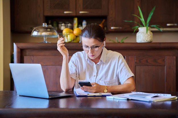 Thuiswerkplek vrouw van middelbare leeftijd met een koptelefoon die werkt met een laptop