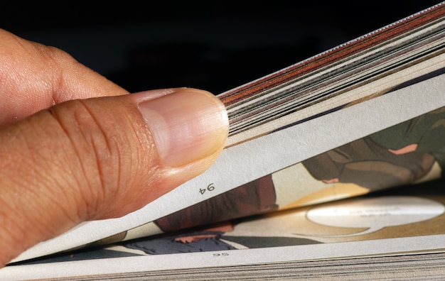 A thumb flipping pages of a comic book, selected focus.