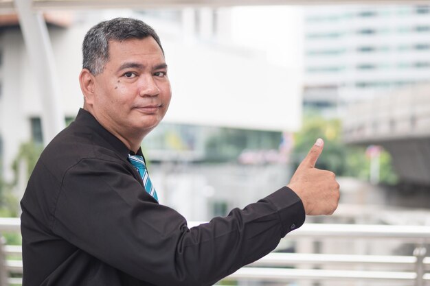 Thumb up from successful old business man portrait of happy strong successful southeast asian businessman pointing showing thumb up good ok hand gesture 50s old south east asian man model