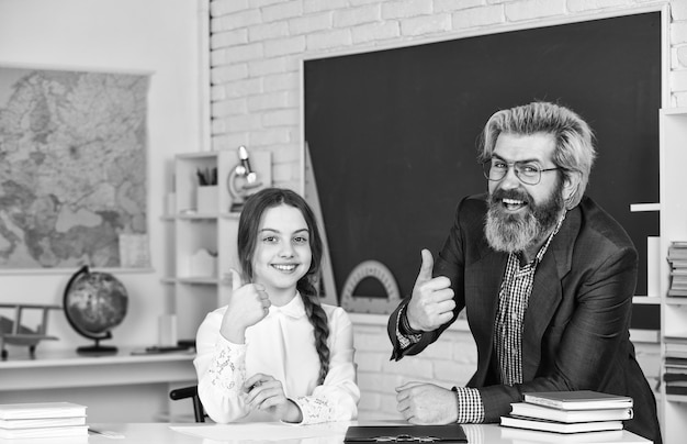 Thumb up for success knowledge day concept child with teacher in classroom at school happy teachers day teacher and schoolgirl on lesson back to school Little girl and man against blackboard