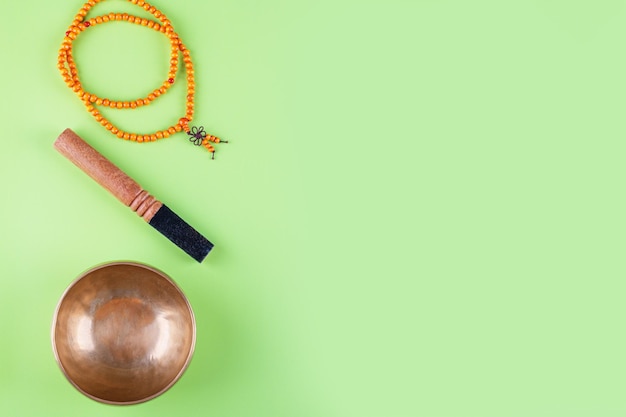 Tibetan singing bowl with stick mala beads strands used during mantra meditations on green stone background