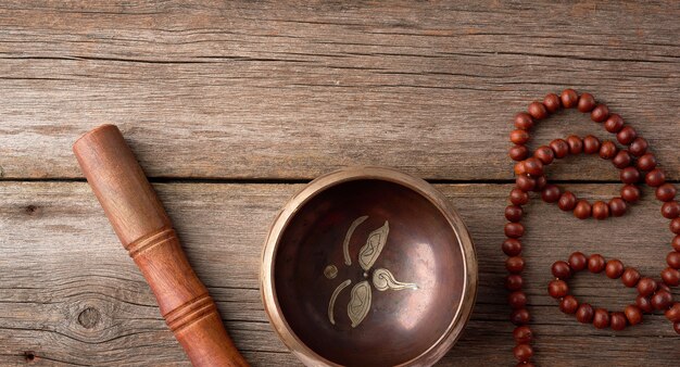 Tibetan singing copper bowl with a wooden clapper and prayer rosary on a gray wooden table