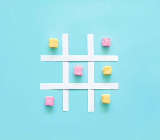 Foto tic tac toe fatto di marshmallow rosa e giallo su sfondo blu.