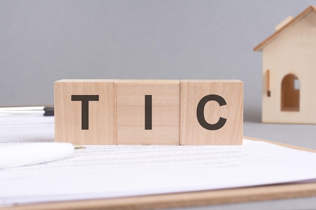 Photo tic text made of wooden blocks on gray background with a small wooden model house