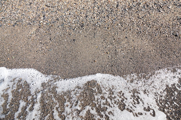 The tide of sea water with foam on the shore with small stony pebbles closeup