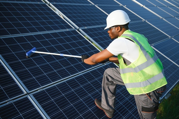 Tidy africanworker is cleaning solar panels with special broom