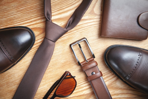 Photo tie, belt, wallet, shoes, sunglasses on the wooden background.