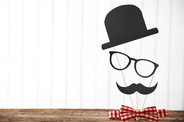 Tie bow with paper mustache hat and glasses on wooden table