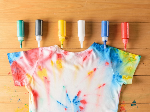 Foto tie dye stijl t-shirt en zes blikjes textielverf op houten tafel.