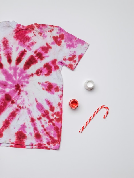 Tie dye style T-shirt, paint and a large red and white candy on a white background. Flat lay.