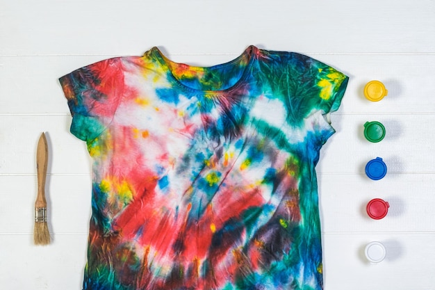 Tie dye tshirt with brush and paint on a white table Flat lay