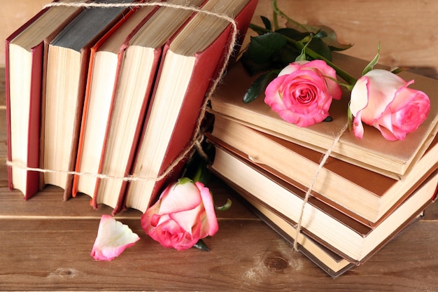 Tied books with pink roses on wooden background