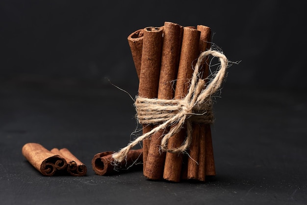 Photo tied bunch of brown cinnamon sticks on a dark background close up