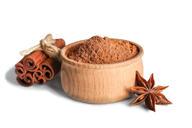 Tied cinnamon sticks and powder in bowl with anise star on white background