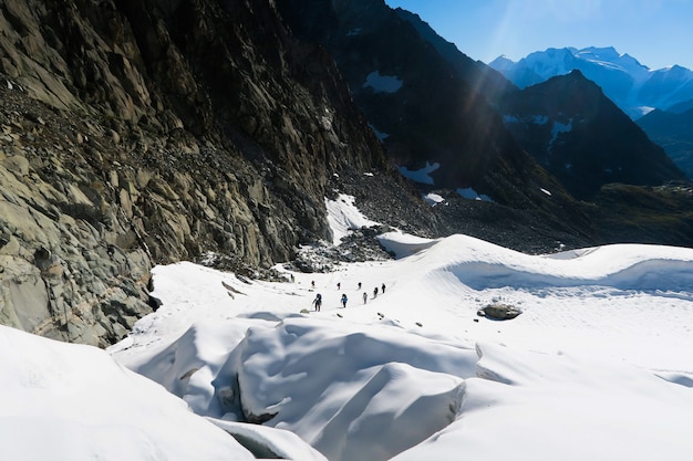 Tied climbers climbing mountain with snow field tied with a rope with ice axes and helmets