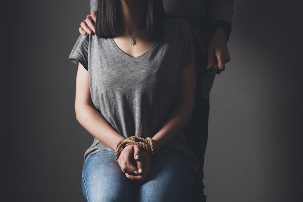 Tied girl and man with a knife in a dark room