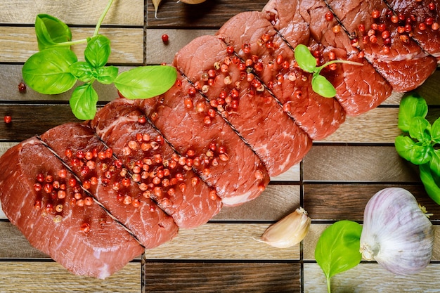 Tied raw beef steak with fresh herbs on wooden board.