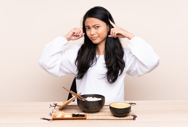 Tiener Aziatisch meisje die Aziatisch die voedsel eten op beige achtergrond wordt geïsoleerd die twijfels en het denken heeft