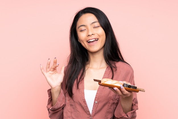 Tiener Aziatisch meisje die sushi bij het roze muur lachen eten