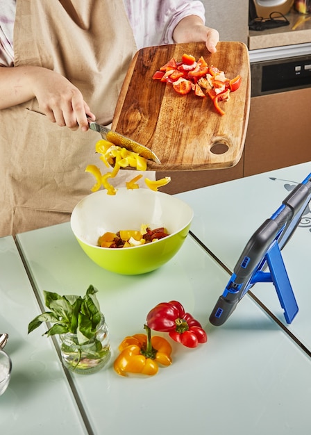 Tiener bereidt salade uit een online tutorial en bekijkt digitaal recept op tablet met aanraakscherm terwijl hij thuis een gezonde maaltijd bereidt