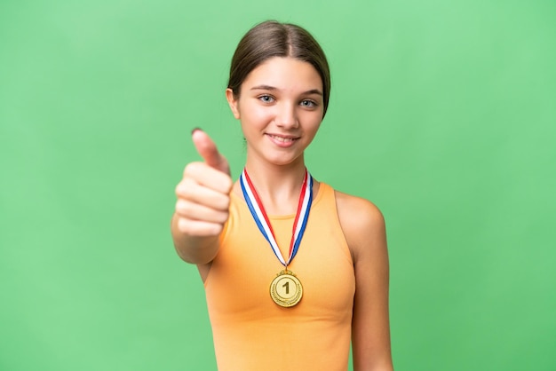 Tiener blank meisje met medailles over geïsoleerde achtergrond met duimen omhoog omdat er iets goeds is gebeurd
