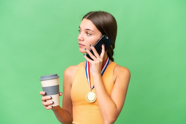 Tiener blank meisje met medailles over geïsoleerde achtergrond met koffie om mee te nemen en een mobiel