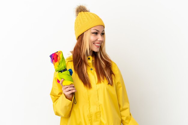 Tiener blond meisje draagt een regendichte jas over een geïsoleerde witte achtergrond en kijkt naar de zijkant