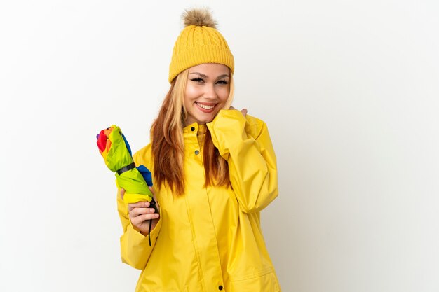 Tiener blond meisje draagt een regendichte jas over geïsoleerde witte achtergrond lachen