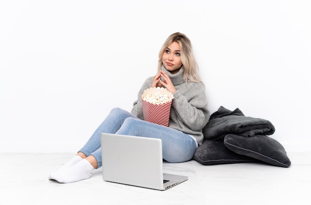 Tiener blond meisje eet popcorn tijdens het kijken naar een film op de laptop iets plannen